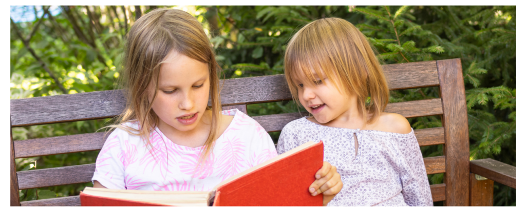 Two young girls reading a book together outdoors, showing how reading aloud for children creates connection and joy.